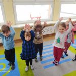 Grupa dzieci podnosi rączki do góry w rytm muzyki