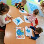 Dzieci przyklejają niebieską bibułę na wydrukowaną planetę