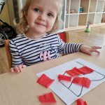 Dziewczynka przykleja czerwoną bibułę do flagi Polski
