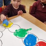 Piotruś wykonuje pracę plastyczną z użyciem farby i balonów