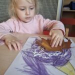 Dzieci wykonują pracę plastyczną z kredkami i liśćmi